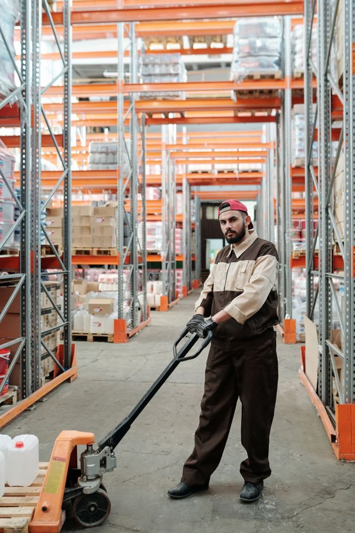 who-we-are Man in uniform using a pallet jack in a well-organized warehouse storeroom.